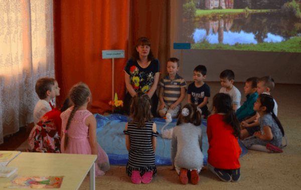 Children and teacher sit on the floor around the “Lake of Kindness”