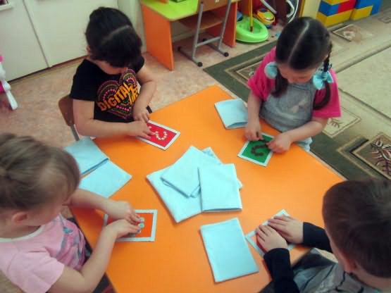 Дети сидят за столом перед ними карточки с цифрами и листы картона