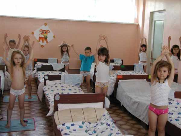Children stand with their hands raised by their beds