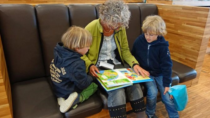 На фото женщина на диване читает книжку с детьми.
