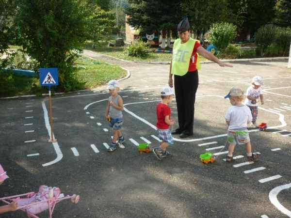 A teacher in a guard costume, children with cars, road markings on the playground